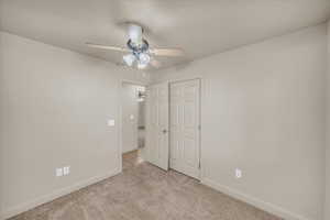 Unfurnished bedroom with ceiling fan, light colored carpet, and a closet