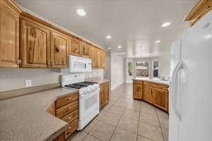 Kitchen featuring sink, white appliances, light tile patterned flooring, decorative light fixtures, and a chandelier