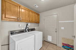 Washroom with cabinets, light tile patterned flooring, a textured ceiling, and washer and clothes dryer