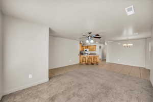 Unfurnished living room with ceiling fan with notable chandelier, light colored carpet, and a textured ceiling