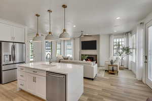 Kitchen with a center island with sink, sink, appliances with stainless steel finishes, decorative light fixtures, and white cabinetry