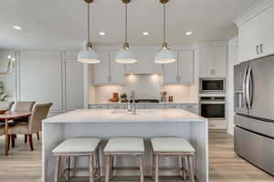 Kitchen featuring white cabinetry, sink, hanging light fixtures, stainless steel appliances, and a center island with sink