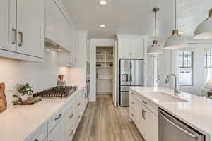 Kitchen featuring stainless steel appliances, sink, white cabinets, light hardwood / wood-style floors, and hanging light fixtures