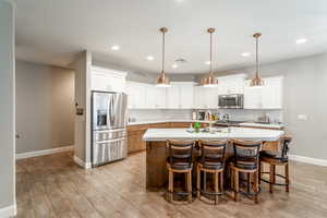 Kitchen featuring appliances with stainless steel finishes, a kitchen island with sink, hanging light fixtures, and white cabinets