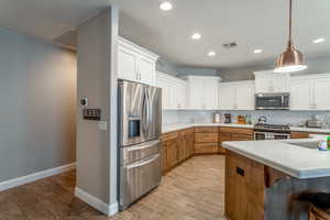 Kitchen featuring stainless steel appliances, decorative light fixtures, decorative backsplash, and white cabinets