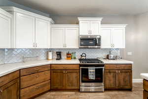 Kitchen with tasteful backsplash, appliances with stainless steel finishes, and white cabinets