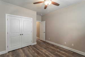 Unfurnished bedroom with a textured ceiling, dark wood-type flooring, a closet, and ceiling fan