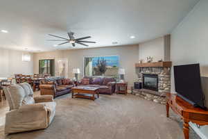 Living room with ceiling fan, a fireplace, carpet floors, and a textured ceiling