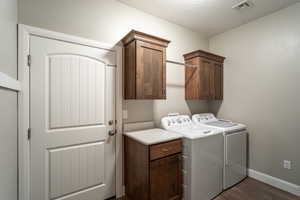 Laundry area featuring cabinets, dark hardwood / wood-style floors, a textured ceiling, and washing machine and clothes dryer