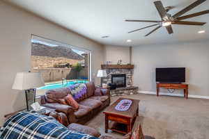 Carpeted living room featuring a stone fireplace and ceiling fan