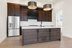 Kitchen featuring pendant lighting, high end refrigerator, dark brown cabinetry, and light hardwood / wood-style flooring