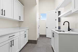 Kitchen featuring light tile patterned flooring, light stone countertops, sink, and white cabinets