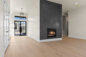 Foyer featuring light hardwood / wood-style flooring, an inviting chandelier, a towering ceiling, a fireplace, and french doors