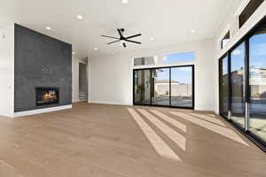 Unfurnished living room featuring light hardwood / wood-style flooring, a large fireplace, and ceiling fan