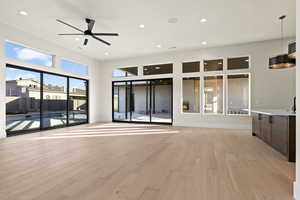 Unfurnished living room with ceiling fan, a towering ceiling, and light hardwood / wood-style floors