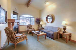 Living room featuring a tile fireplace, carpet, and vaulted ceiling with beams