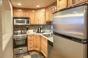 Kitchen with tasteful backsplash, sink, light stone counters, and appliances with stainless steel finishes