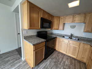 Kitchen with sink, a textured ceiling, dark stone counters, hardwood / wood-style floors, and black appliances