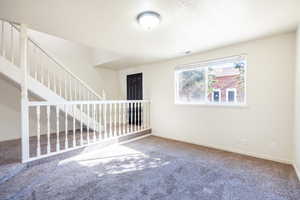 Empty room featuring a textured ceiling, visible vents, baseboards, stairway, and carpet