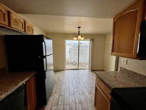 Kitchen featuring light hardwood / wood-style flooring, a notable chandelier, black appliances, a textured ceiling, and decorative light fixtures