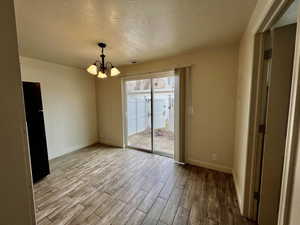 Unfurnished dining area with a notable chandelier, light hardwood / wood-style floors, and a textured ceiling