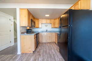 Kitchen with light wood-style floors, a textured ceiling, black appliances, light brown cabinets, and a sink