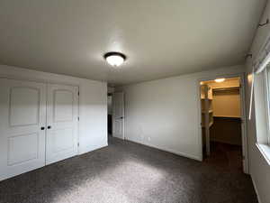 Unfurnished bedroom with dark colored carpet, a spacious closet, a textured ceiling, and a closet