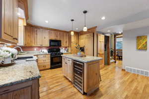 Kitchen with wine cooler, a center island, hanging light fixtures, light hardwood / wood-style floors, and black appliances