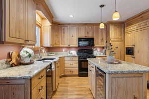 Kitchen featuring decorative light fixtures, sink, wine cooler, a center island, and black appliances