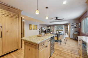 Kitchen featuring hanging light fixtures, light wood-type flooring, light stone countertops, and a kitchen island