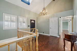 Foyer entrance with dark hardwood / wood-style floors, an inviting chandelier, high vaulted ceiling, and a skylight