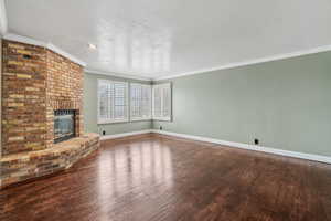 Living room featuring crown molding, hand scraped wood flooring, a brick fireplace, and a textured ceiling