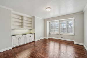 In-home office with dark wood-type flooring, ornamental molding, and a textured ceiling