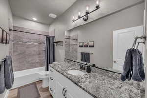 Full bathroom with wood-type flooring, vanity, shower / bathtub combination with curtain, and toilet