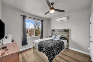 Bedroom with a wall mounted air conditioner, hardwood / wood-style floors, and ceiling fan