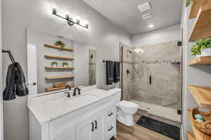 Bathroom featuring toilet, a shower with shower door, a textured ceiling, vanity, and hardwood / wood-style flooring