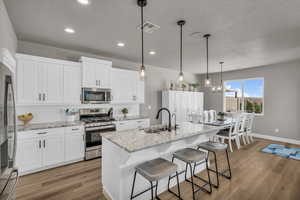 Kitchen featuring stainless steel appliances, white cabinetry, pendant lighting, and an island with sink