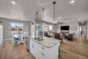 Kitchen featuring pendant lighting, sink, white cabinetry, a kitchen island with sink, and light stone countertops