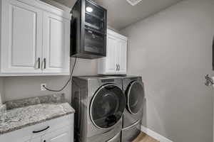 Laundry area with light hardwood / wood-style flooring, washing machine and dryer, and cabinets