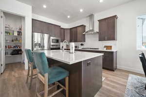 Kitchen with wall chimney range hood, sink, appliances with stainless steel finishes, a kitchen island with sink, and backsplash