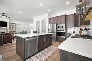 Kitchen featuring sink, stainless steel appliances, tasteful backsplash, light hardwood / wood-style floors, and a center island with sink