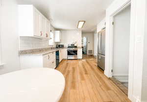 Kitchen with white cabinetry, stainless steel appliances, decorative backsplash, and light wood-type flooring