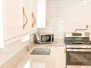 Kitchen featuring sink, light stone counters, tasteful backsplash, appliances with stainless steel finishes, and white cabinets