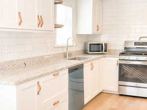 Kitchen featuring sink, stainless steel appliances, tasteful backsplash, light stone counters, and white cabinets