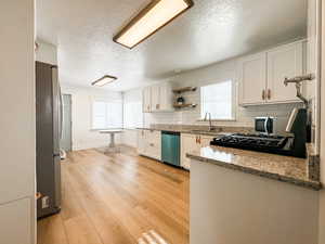 Kitchen with sink, white cabinets, light stone counters, stainless steel appliances, and light hardwood / wood-style flooring