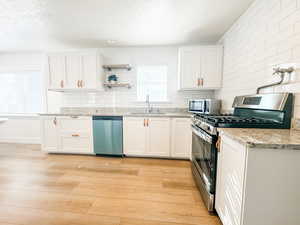 Kitchen featuring appliances with stainless steel finishes, sink, white cabinets, backsplash, and light hardwood / wood-style flooring