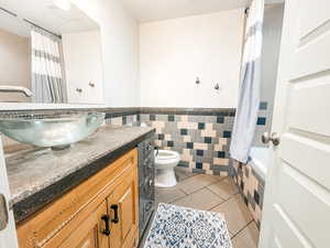 Full bathroom with tile walls, vanity, shower / bath combination with curtain, tile patterned floors, and toilet