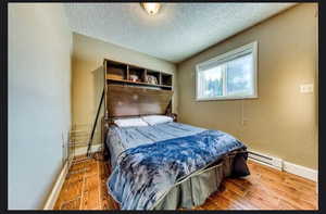 Bedroom featuring hardwood / wood-style flooring, a textured ceiling, and baseboard heating