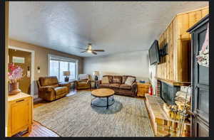 Living room with hardwood / wood-style flooring, ceiling fan, a brick fireplace, and a textured ceiling