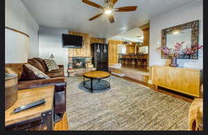 Living room featuring a brick fireplace, hardwood / wood-style flooring, a textured ceiling, and ceiling fan